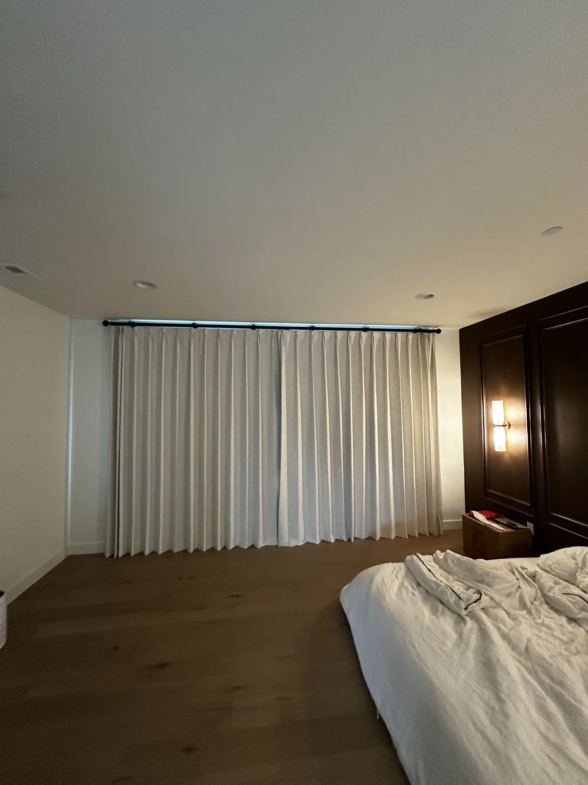 Light-colored floor-length drapery closed across a bedroom window on a dark rod