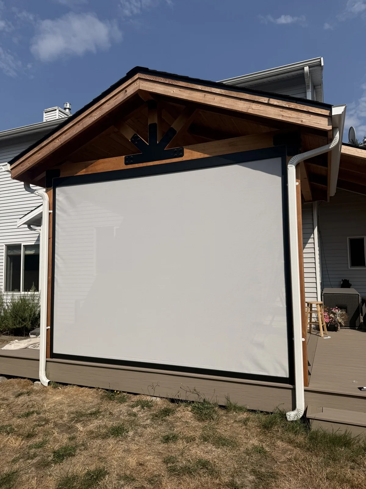 Light-colored outdoor shade lowered between black side tracks on a timber-framed covered patio