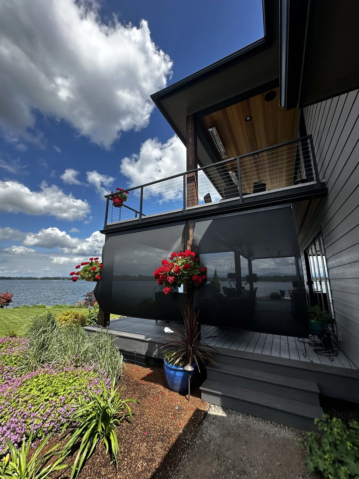 Dark outdoor shades lowered around a waterfront patio with hanging flower baskets