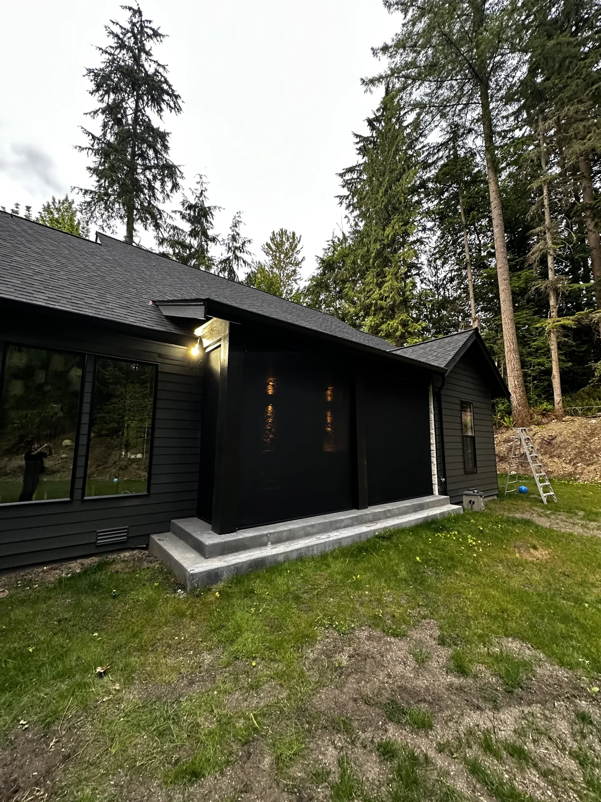 Dark outdoor shades enclosing a covered patio beside a wooded yard